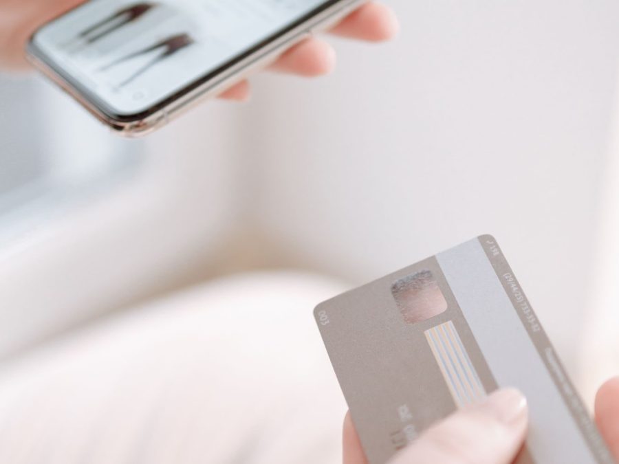 Mâini care țin un smartphone și un card pentru cumpărături online