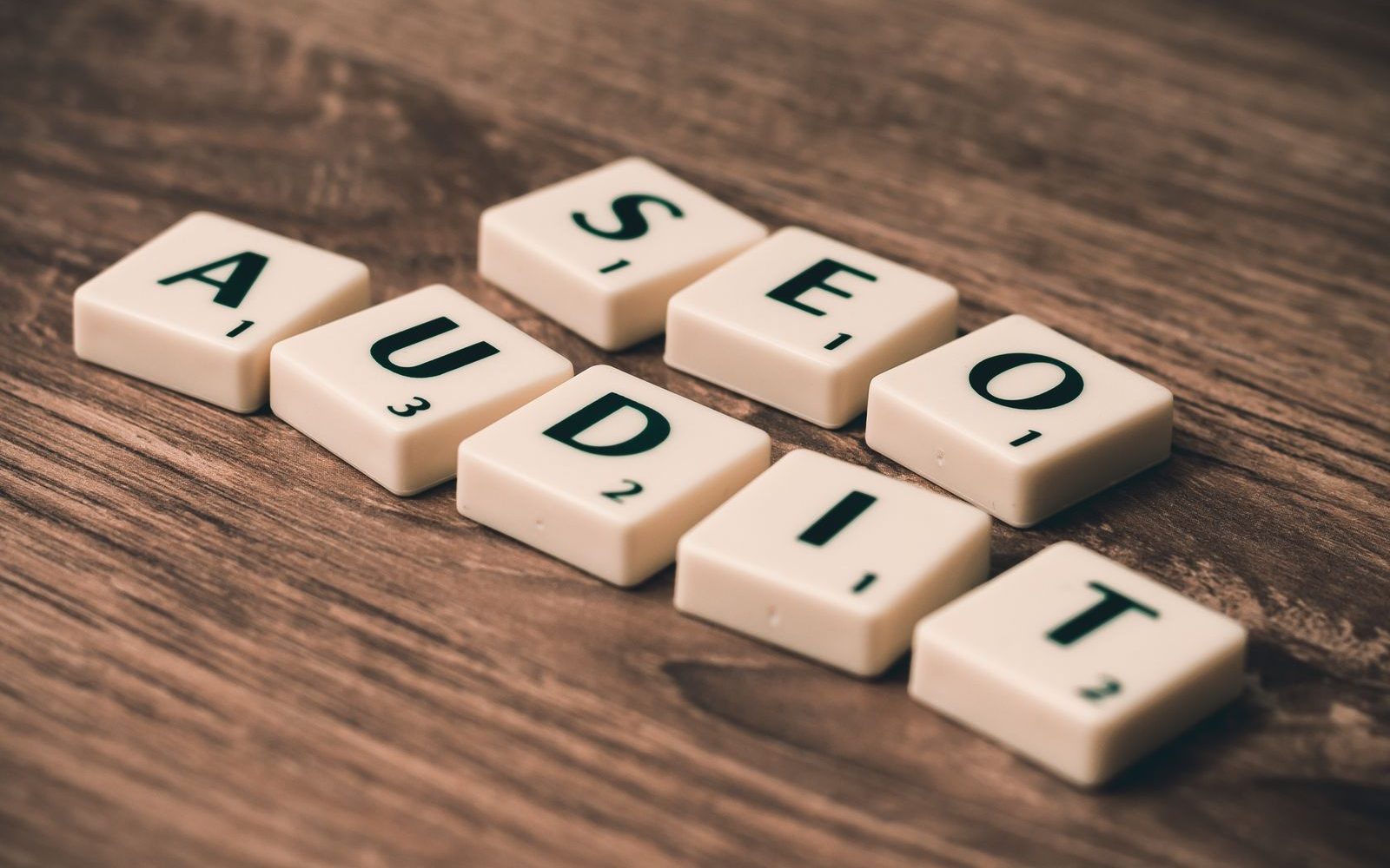 Litere de Scrabble care formează „SEO Audit”, pe o masă de lemn