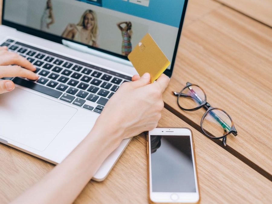 Persoană care plătește online cu cardul, pe laptop, cu un smartphone alături