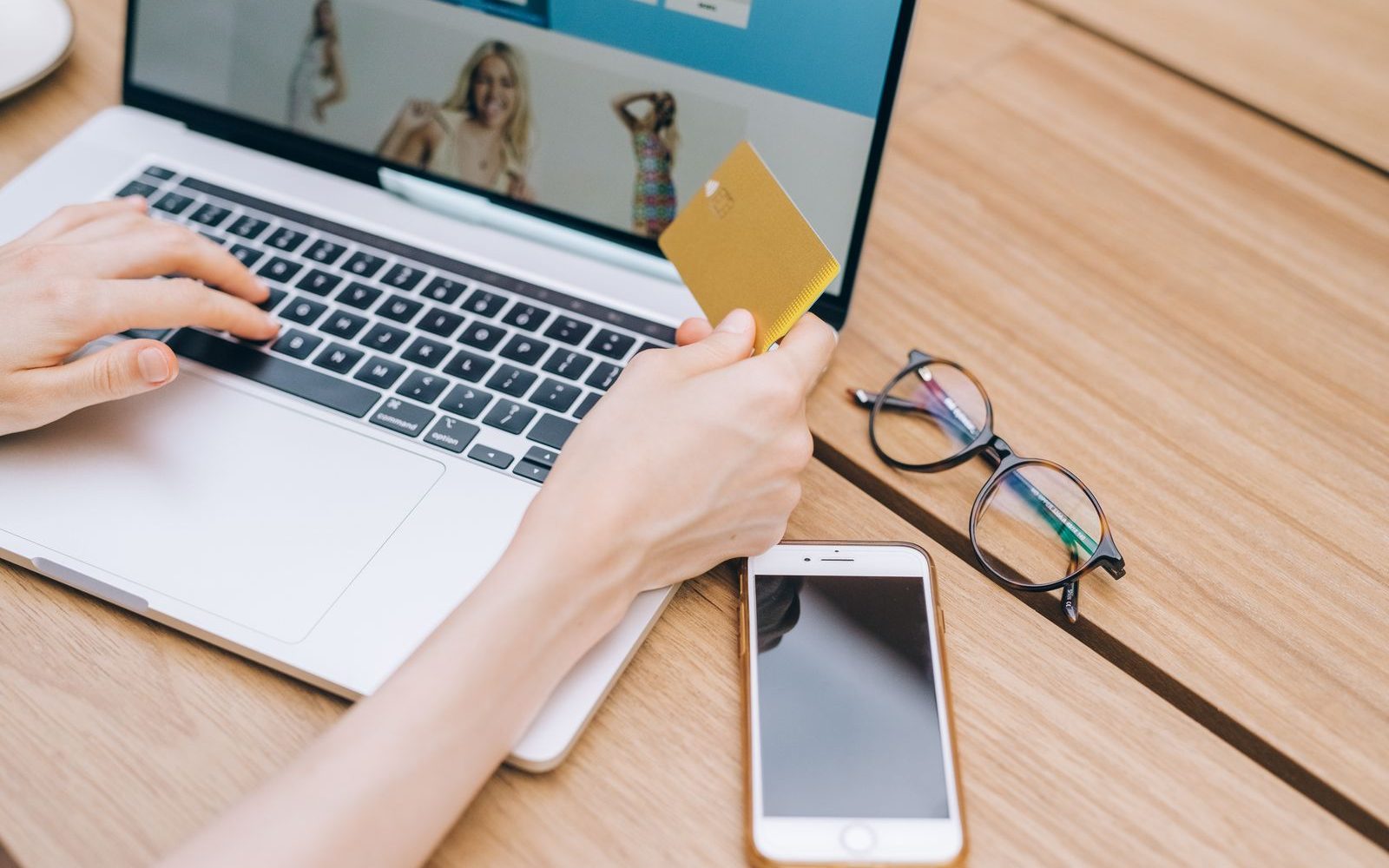 Persoană care plătește online cu cardul, pe laptop, cu un smartphone alături