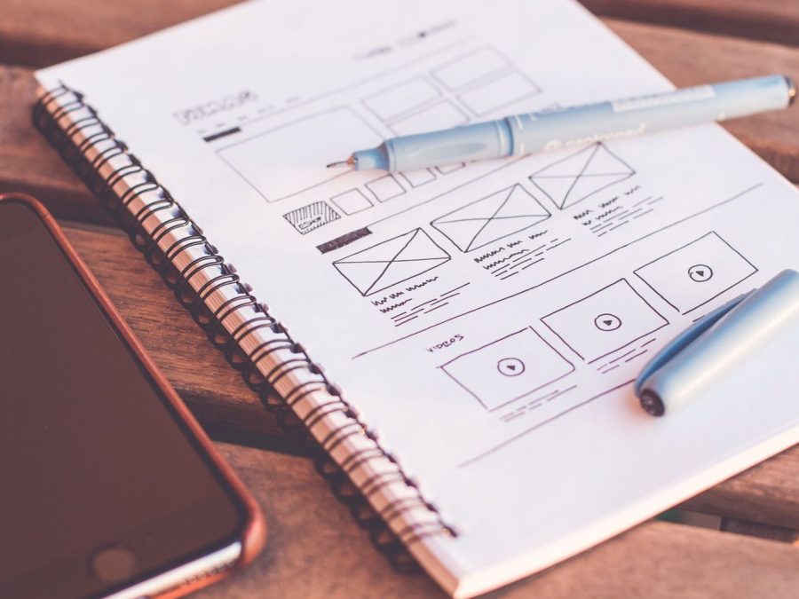 Caiet cu schițe de wireframe și un smartphone pe un birou din lemn