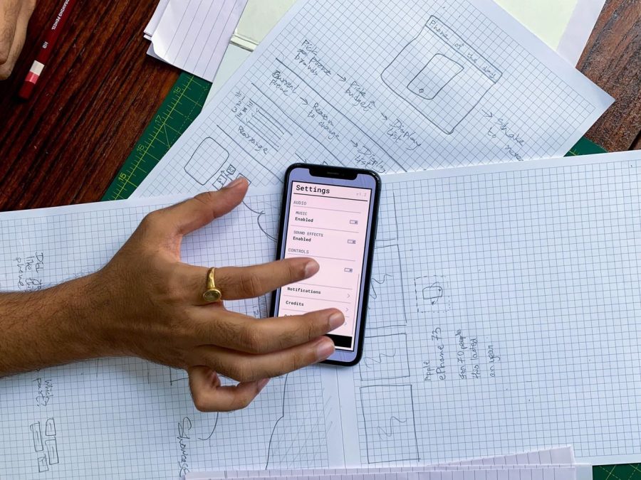Mână care ține un smartphone peste schițe de design pentru o aplicație