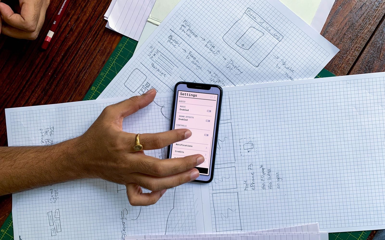 Mână care ține un smartphone peste schițe de design pentru o aplicație
