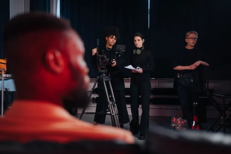 Echipă de filmare în studio, cu cameră pe trepied și operatori care pregătesc o scenă